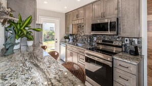 A modern kitchen with granite countertops, stainless steel appliances, and a stone backsplash. - 400 South - Unit C (Cocoa Beach)