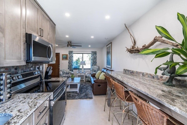 A modern kitchen with granite countertops, stainless steel appliances, and a bar area with wicker chairs.