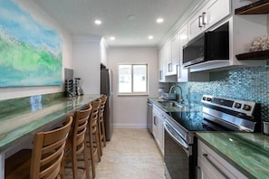 A kitchen with a bar area, a refrigerator, a microwave, a stove, and a window.