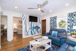 A modern living room with a ceiling fan, a blue sofa, a coffee table, and a wall-mounted TV. - 400 South - Unit G (Cocoa Beach)