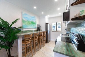 A modern kitchen with a bar area, a large painting, and a potted plant. - 400 South - Unit G (Cocoa Beach)