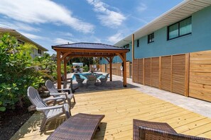 Un jardin avec une terrasse en bois, des chaises longues, une piscine et une pergola.