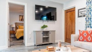 Een moderne woonkamer met een flatscreen televisie, een houten salontafel, een bank en een deur naar een andere kamer.