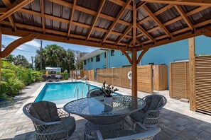 Un espace extérieur abrité avec une piscine, des meubles en osier et un bâtiment bleu en arrière-plan.