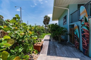 A pathway leading to a building with a mural, surrounded by lush greenery and a clear sky.
