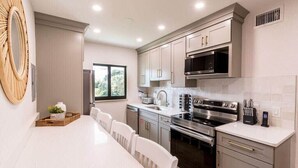 Una cocina moderna con armarios blancos, electrodomésticos de acero inoxidable y un comedor con una mesa y sillas blancas.