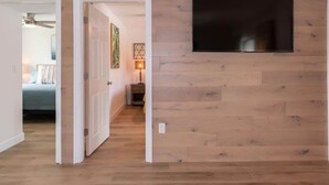 Un pasillo con piso de madera, una puerta que da a un dormitorio y un televisor montado en la pared.