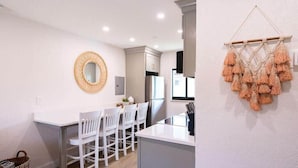 Una cocina moderna con armarios blancos, una isla central con asientos y un colgador de macramé en la pared.