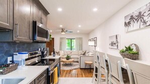 A modern kitchen with a microwave, stove, and cabinets. There is a dining area with a table and chairs. - 400 South - Unit F (Cocoa Beach)