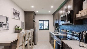 A modern kitchen with dark cabinets, a stainless steel stove, and a window. - 400 South - Unit F (Cocoa Beach)