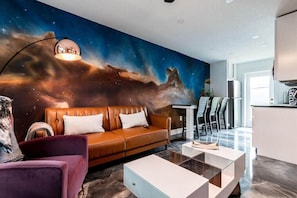 A modern living room with a large wall mural, a brown leather sofa, a purple armchair, and a glass coffee table.