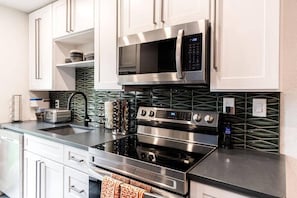 A modern kitchen with stainless steel appliances, white cabinets, and a green patterned backsplash.
