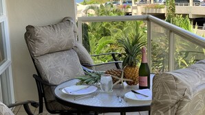 Ein Balkon mit Tisch für zwei Personen, ausgestattet mit einer Champagnerflasche, einer Ananas und einem Glas Wasser.