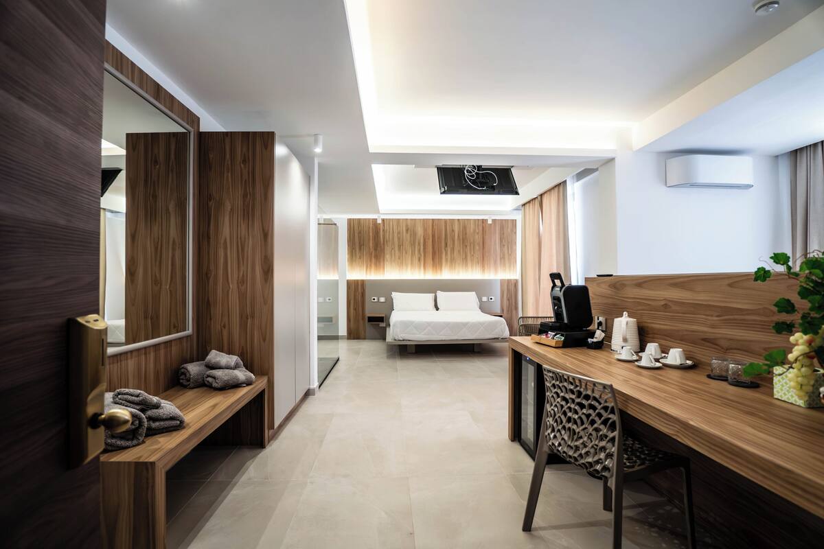 Une chambre d’hôtel moderne avec un bureau en bois, un lit, une banquette avec des serviettes et un grand miroir.