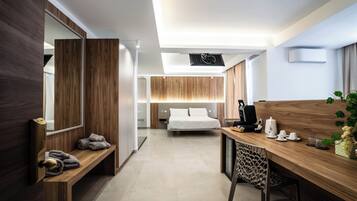 A modern hotel room with a wooden desk, a bed, a bench with towels, and a large mirror.