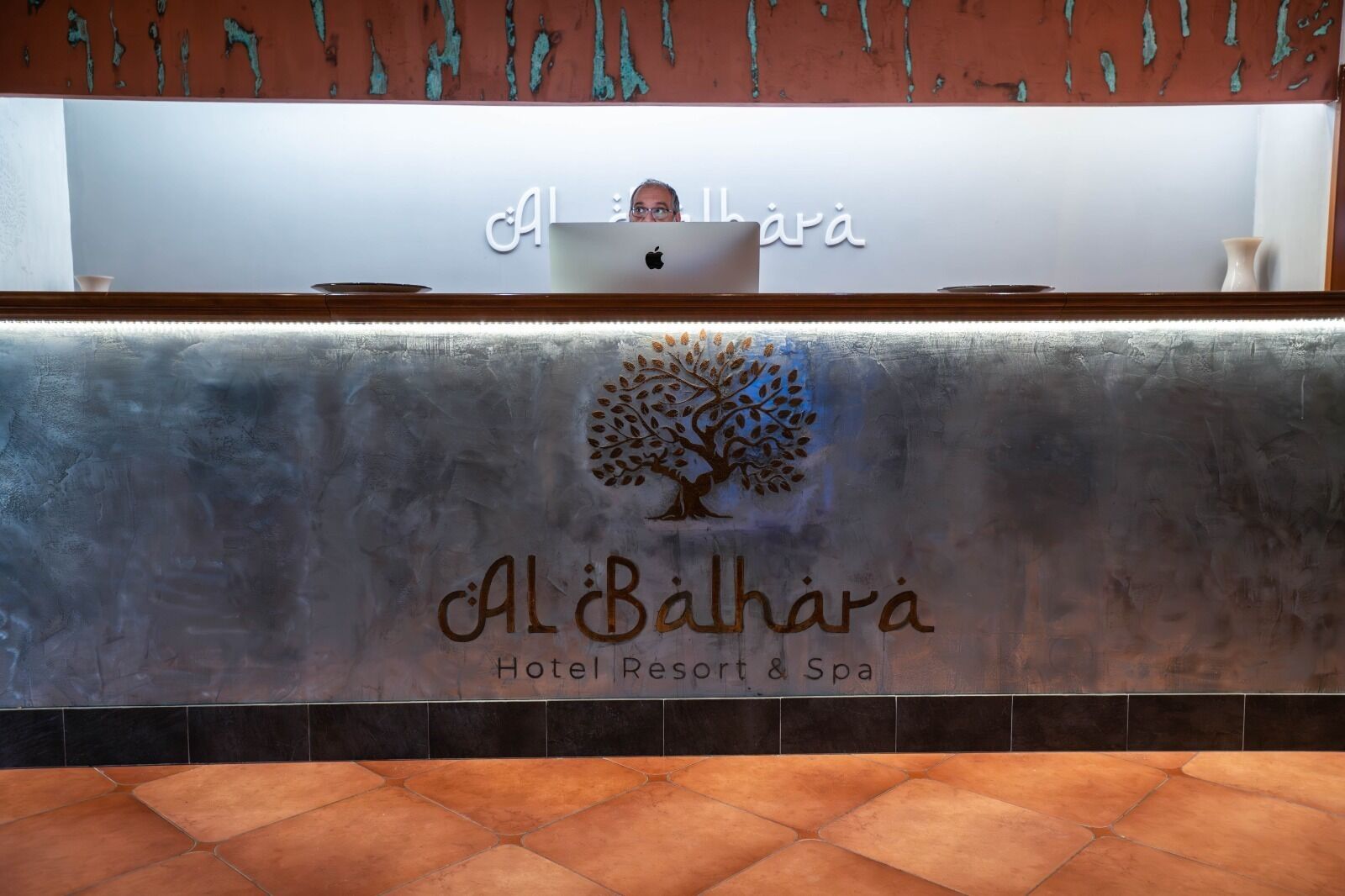 Un mostrador de recepción con un logotipo que muestra un árbol y el nombre "Al Bahara Hotel Resort & Spa" en árabe.
