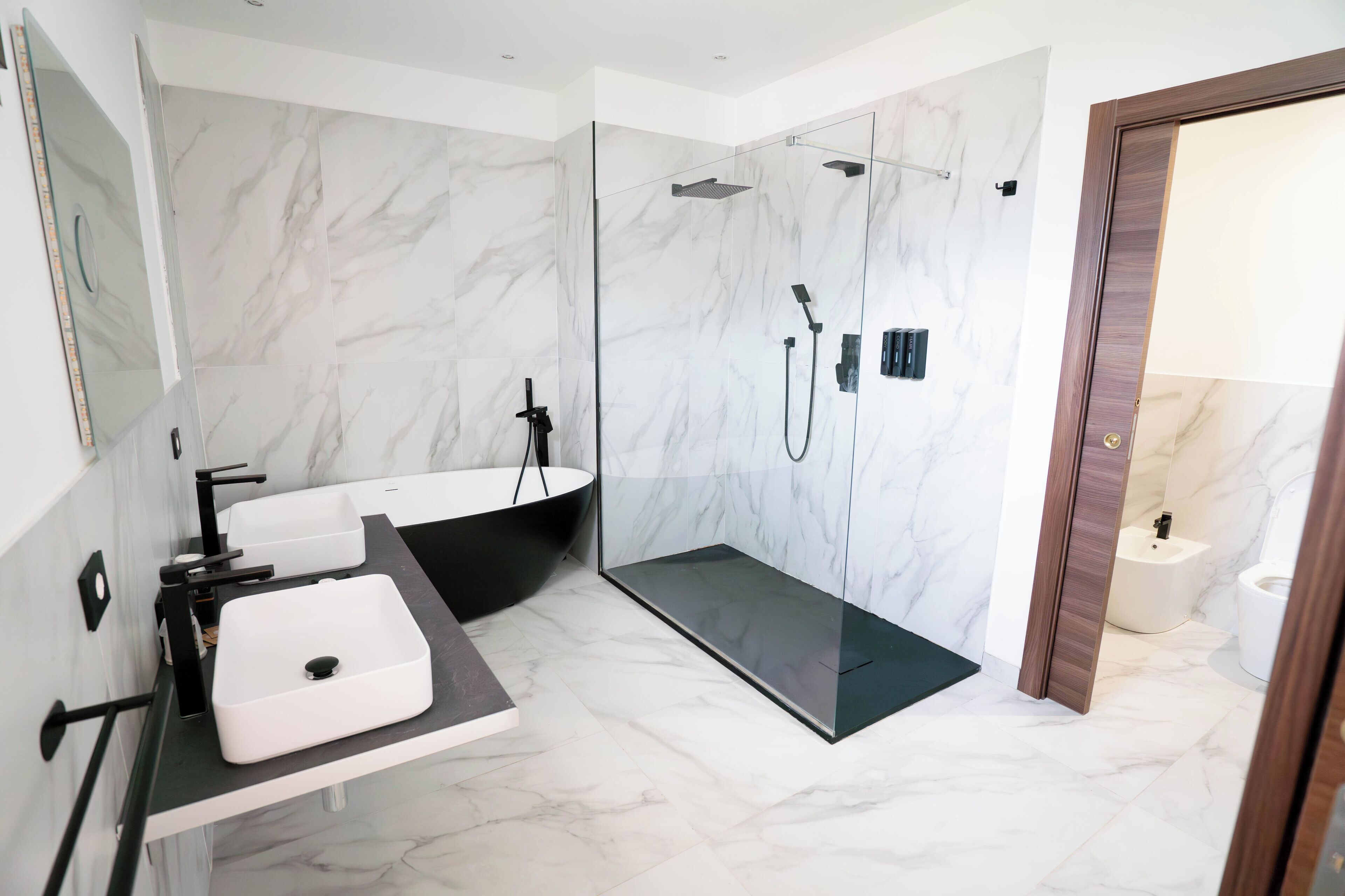 A modern bathroom with a large white sink, a black bathtub, and a glass-enclosed shower area.