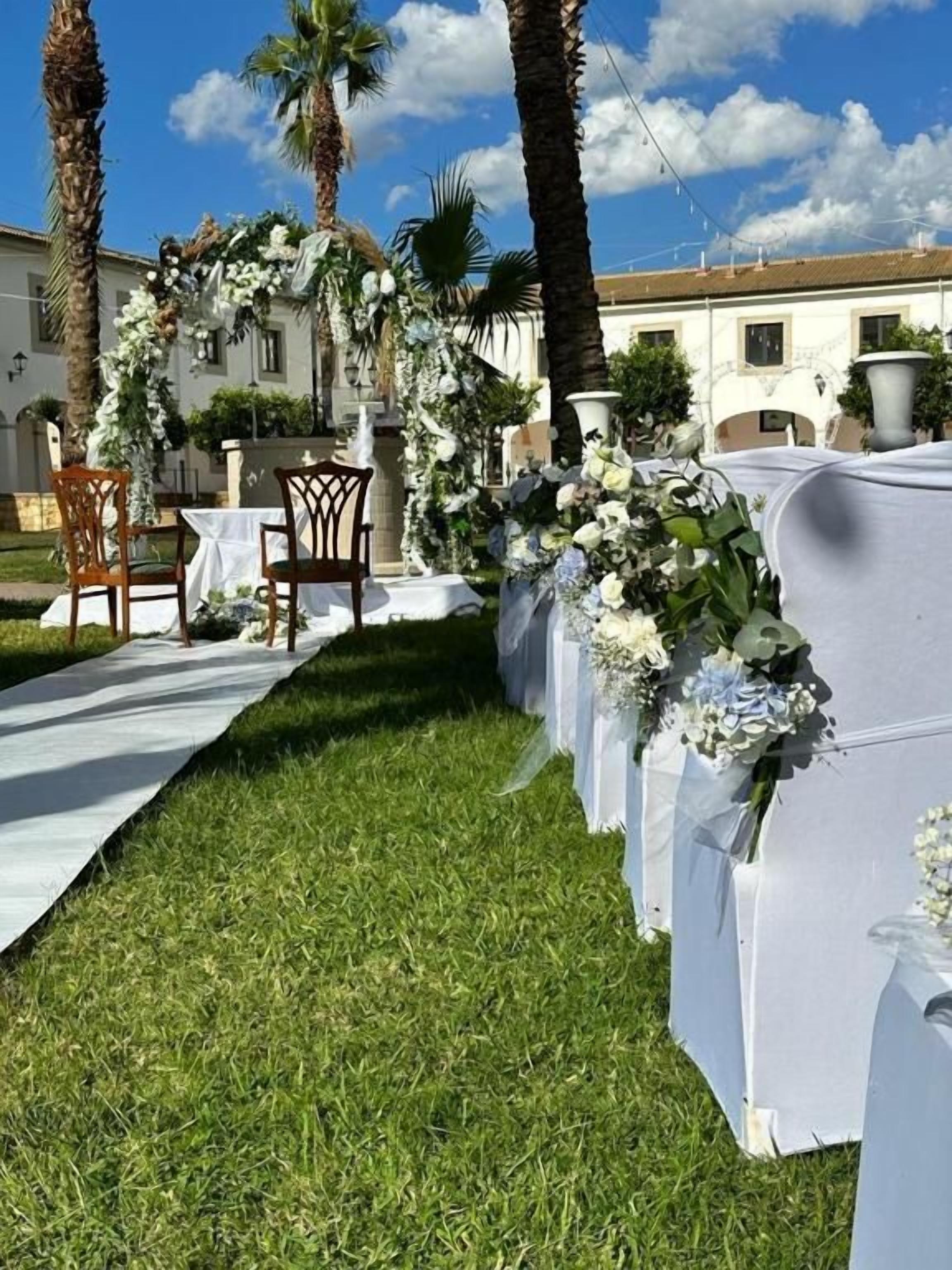 A wedding aisle with white drapes and floral arrangements, leading to a building with a white facade.