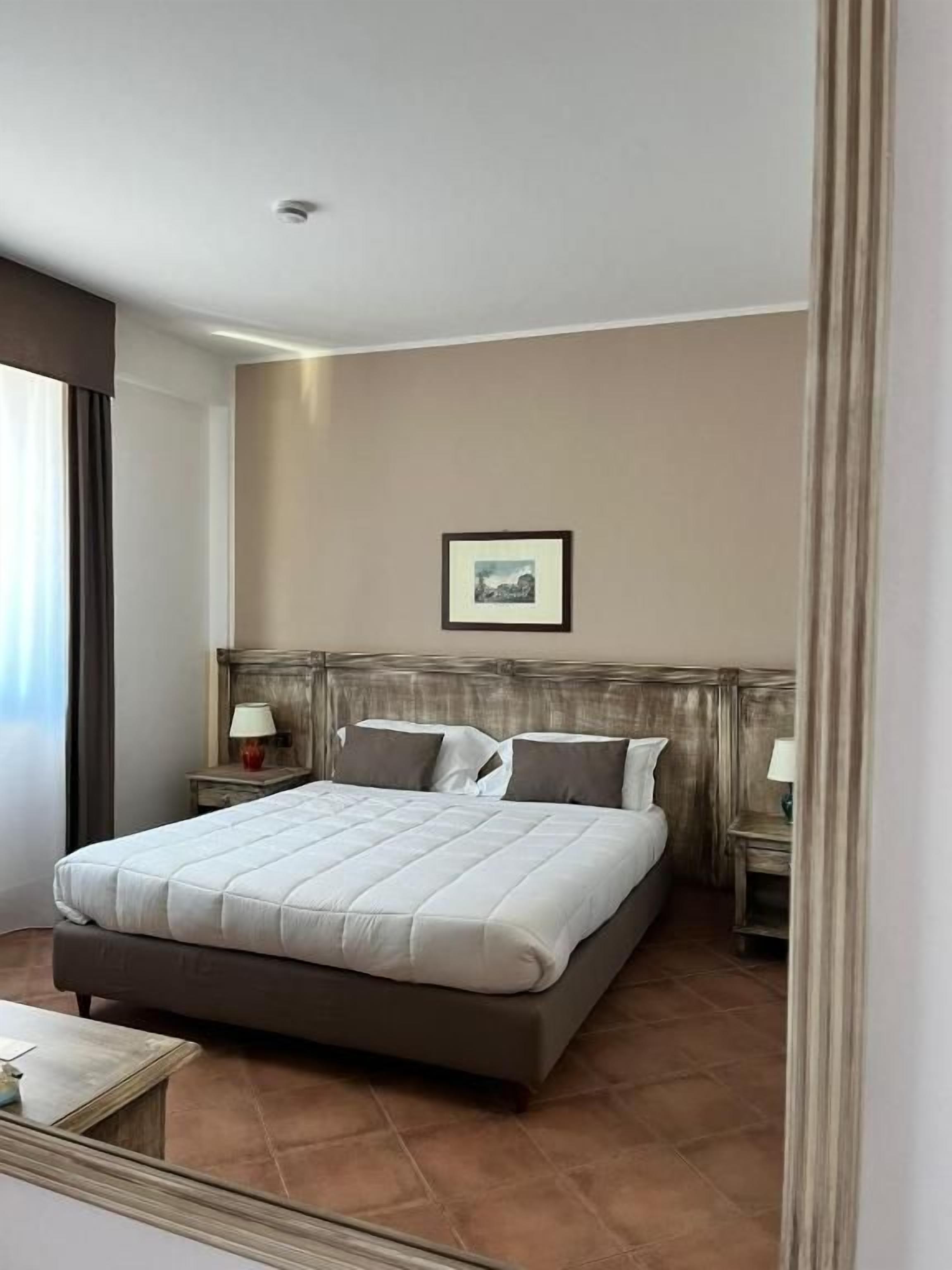 A hotel room with a large bed, two bedside tables with lamps, a framed picture on the wall, and a window with curtains.