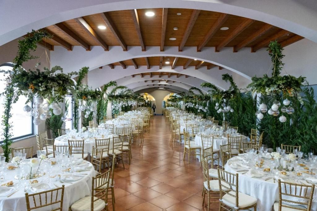 Una sala da banchetto con tavoli rotondi, tovaglie bianche e sedie dorate.