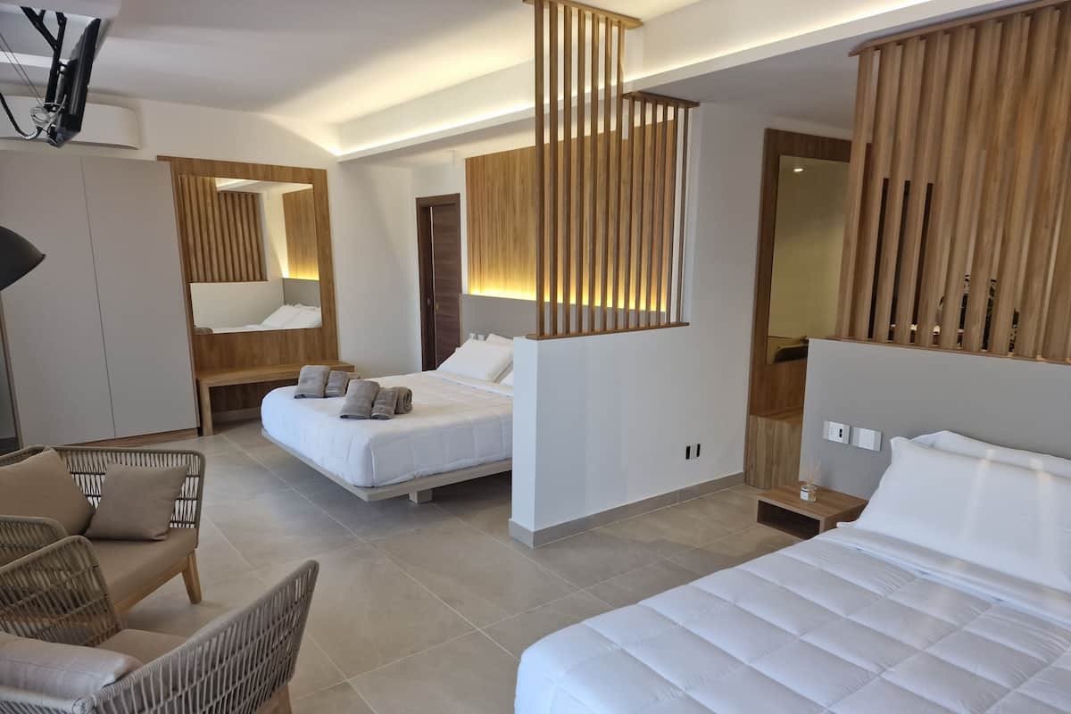 Une chambre d’hôtel moderne avec un grand lit, un canapé, un fauteuil et une cloison en bois.