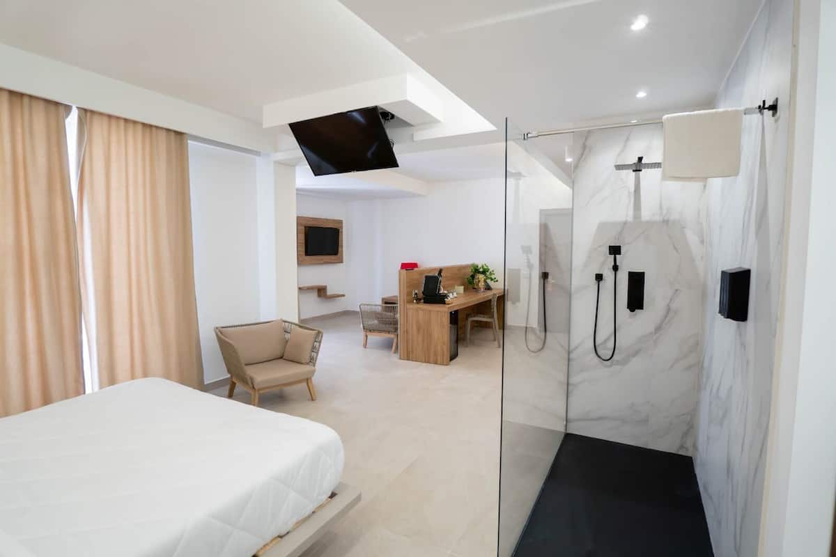 Une chambre d’hôtel moderne équipée d’un lit, d’un bureau, d’une chaise, d’une douche et d’un téléviseur fixé au mur.
