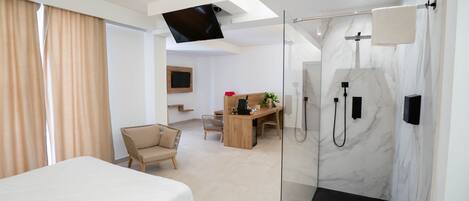 Une chambre d’hôtel moderne équipée d’un lit, d’un bureau, d’une chaise, d’une douche et d’un téléviseur fixé au mur.