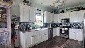 A kitchen with white cabinets, a stainless steel oven, a microwave, and a sink. - OBX NEW WATERFRONT DESIGNER HOME WITH DOCK. GORGEOUS AND COMFY INSIDE AND OUT! (Kill Devil Hills)