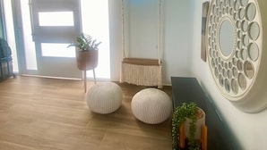 Ein modernes Wohnzimmer mit einer hängenden Makramee-Leuchte, einem Neon-Schild, einem dekorativen Wandspiegel und zwei runden Poufs auf Holzboden.