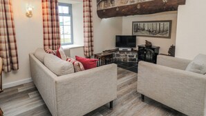 A living room with a stone fireplace, a television, and a window with curtains. - Carthouse (Weston-super-Mare)