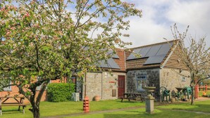 A stone building with a red door, a small window, and a garden with a tree and a picnic table. - Carthouse (Weston-super-Mare)