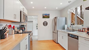 A modern kitchen with white cabinets, stainless steel appliances, and a wooden countertop. - The Red Lodge - Unique Gem Near Lakes with Game Room and Hot Tub! (Elkhorn)
