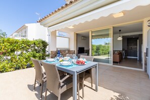 An outdoor dining area with wicker chairs and a table set for four, overlooking a garden and a building with a tiled roof.