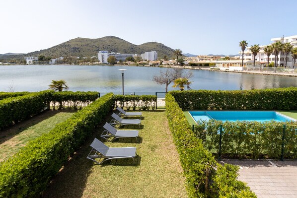 A poolside area with lounge chairs, a swimming pool, and a view of a lake with buildings in the background.