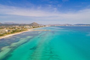 An aerial view of a coastal area with clear turquoise waters, a beach, and a mountain in the background.