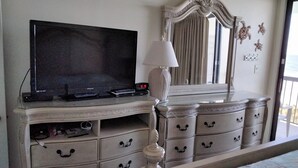 Una camera da letto con televisione, comò e uno specchio grande.