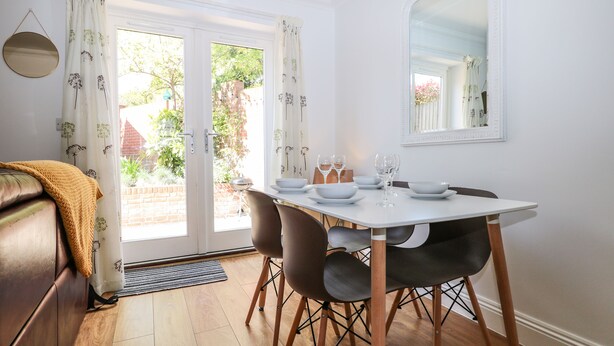 A dining area with a table set for four, a sofa, and a large mirror on the wall. - Trinity Cottage (Christchurch)