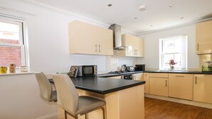A modern kitchen with a central island, bar stools, a microwave, and a stove. - Trinity Cottage (Christchurch)