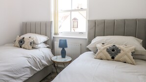 A bedroom with two beds, a window, and a lamp. - Trinity Cottage (Christchurch)