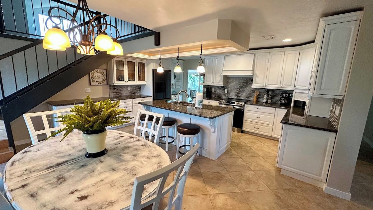 A modern kitchen with a central island, white cabinetry, and a dining area with a marble table.