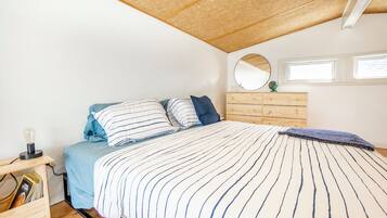 Une chambre à coucher avec un lit, une commode en bois, un miroir rond et une petite table avec une lampe.
