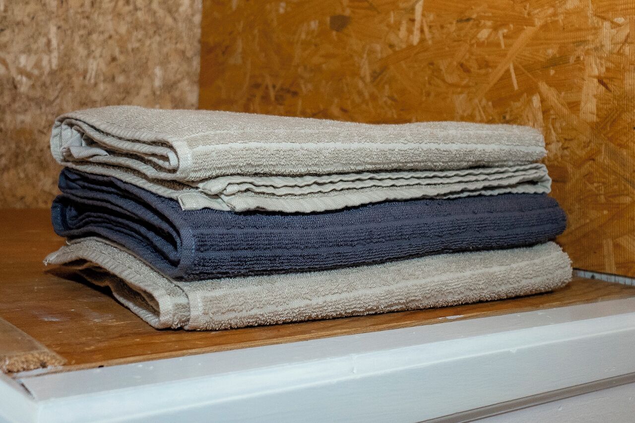 A stack of folded towels in various colors on a wooden shelf.