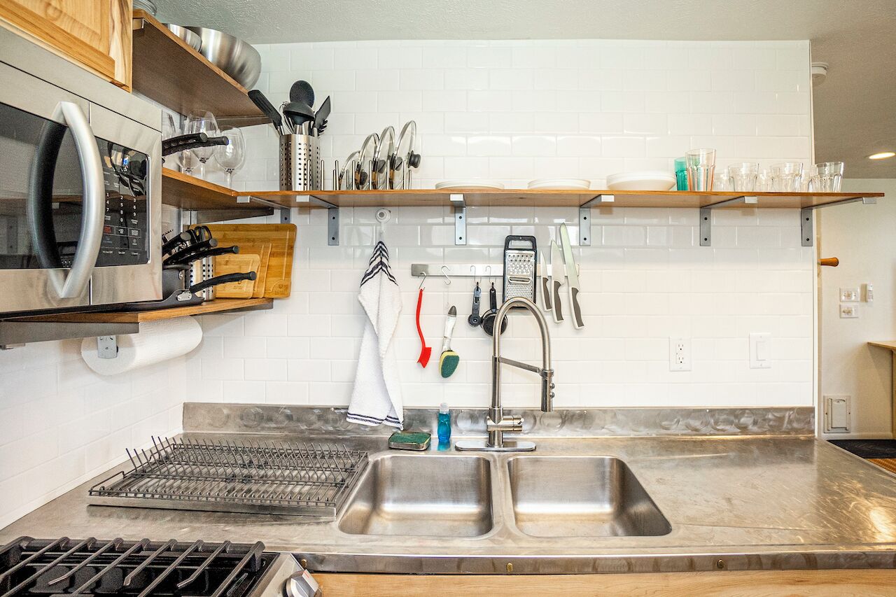 A modern kitchen with stainless steel appliances, a double sink, and wooden shelves.