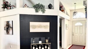 Een modern interieur met een zwarte accentmuur, een ingelijst abstract schilderij, een decoratieve metalen standaard en een witte deur.