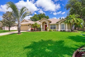 A residential house with a well-maintained lawn, palm trees, and a clear blue sky.