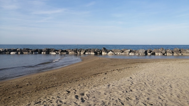 A beach with a rocky breakwater and a sandy shore. - Hotel Luca (Rimini)
