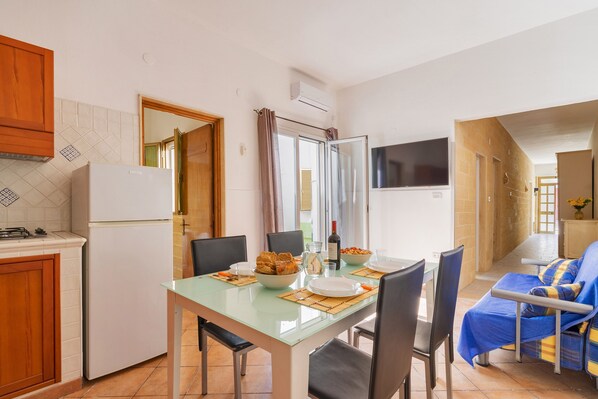 A compact kitchen with a refrigerator, dining table, chairs, and a TV.