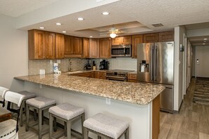 A modern kitchen with granite countertops, wooden cabinets, stainless steel appliances, and bar stools. - Penthouse Paradise 3 bed OF (St. Augustine)