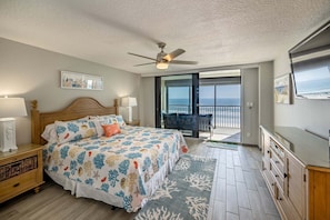 A bedroom with a bed, a ceiling fan, a nightstand, a dresser, and a view of the ocean through a sliding glass door. - Sand Dollar 507 Penthouse Paradise (St. Augustine)