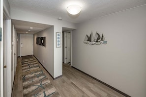 A hallway with a carpet, a door labeled 'BEACH,' and a wall with sailboat decorations. - Sand Dollar 507 Penthouse Paradise (St. Augustine)